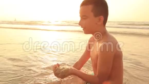 日落或日出时在海上海岸建造沙堡的男孩视频的预览图