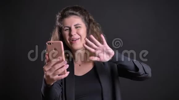 在黑色背景下使用智能手机在可视电话中交谈的超重高加索妇女的特写照片视频的预览图