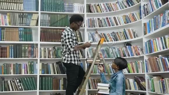 在大学图书馆里站在梯子上为非洲女性寻找书架上的书籍视频的预览图