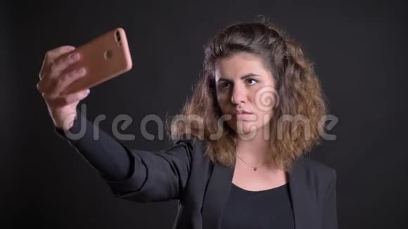 在黑色背景下使用智能手机制作自拍照片的超重高加索妇女的特写肖像视频的预览图