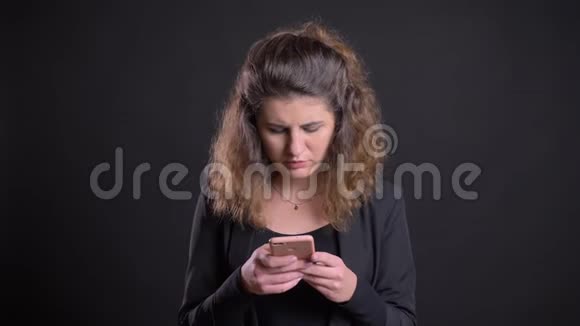 超重的白种人女性观看智能手机并在黑色背景下微笑的特写肖像视频的预览图