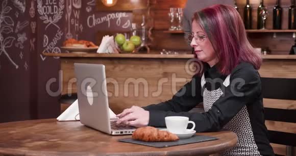 女人一边喝咖啡一边打手提电脑键盘视频的预览图