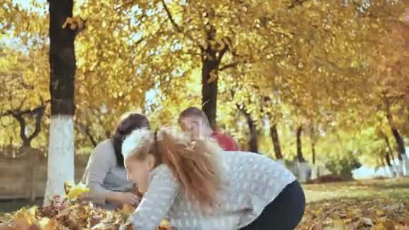在阳光明媚的秋天天气里快乐的一家人在户外玩落叶父母在后台接吻视频的预览图