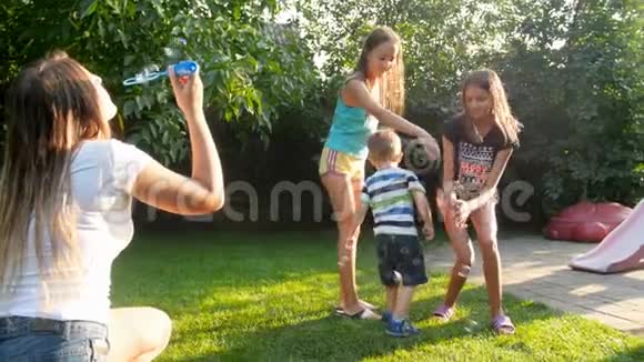 阳光明媚的夏日孩子们在后院花园里飞来飞去开心地笑着抓着肥皂泡的慢镜头视频的预览图