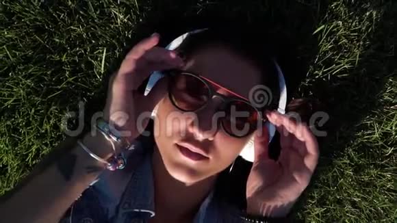 靠近亚洲女孩一边摘下太阳镜一边躺在绿色清新的草地上视频的预览图