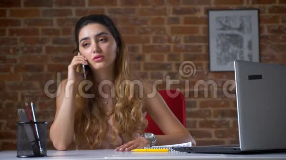 一位美丽而忧心忡忡的白种人女孩正坐在桌面上背景是红砖视频的预览图