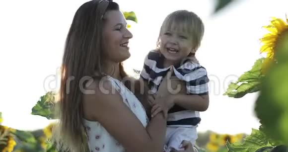 快乐的母亲和小儿子站在一片向日葵的田野里视频的预览图