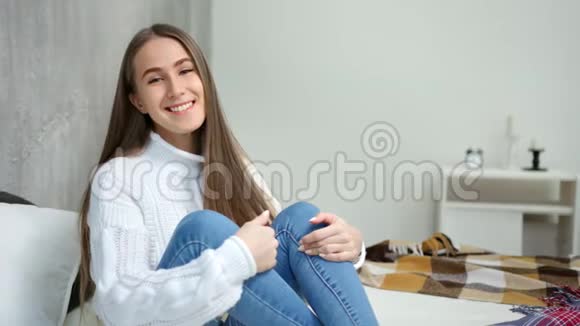 中等镜头肖像笑着舒适的年轻女子坐在床上双手抱着腿视频的预览图