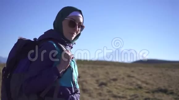 美丽的穆斯林女性旅行者带着背包和眼镜看着相机走向群山视频的预览图
