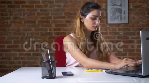 本想在工作场所坐着的白种人漂亮的女人正在用手提电脑工作停下来接电话视频的预览图