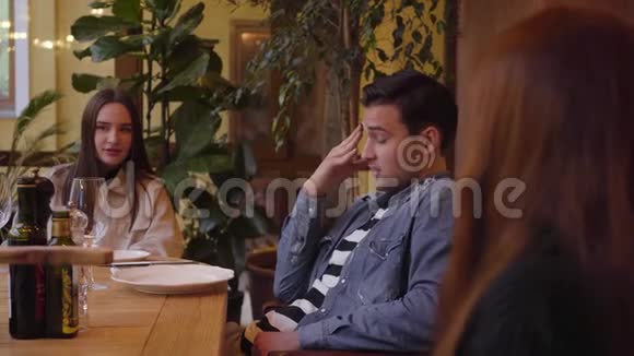 三位朋友在餐桌旁的现代意大利咖啡馆里吃着美味的披萨和喝酒两个年轻妇女和一个视频的预览图