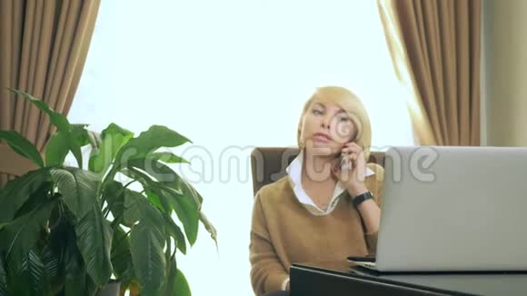 办公室里的女人在打电话看着笔记本电脑视频的预览图