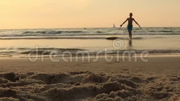 日落时分带着冲浪板在海滩上冲浪的小男孩视频的预览图
