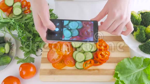 女人手拿着智能手机正在为沙拉拍摄新鲜蔬菜的照片切片在切割板上视频的预览图