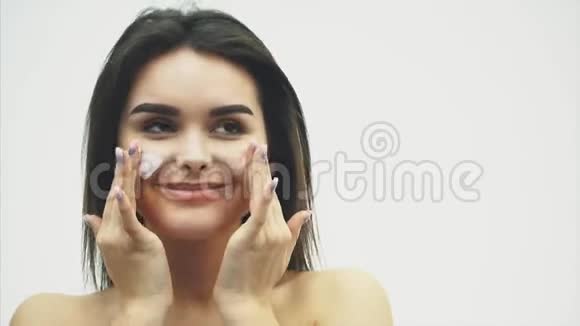 女面护肤迷人的年轻女性在眼睛和瓶子下涂抹奶油的肖像特写视频的预览图
