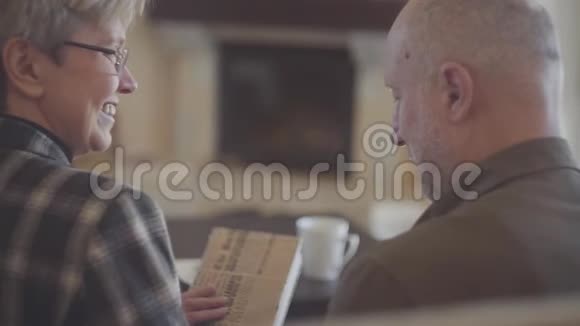 老夫妇的背影男人和女人坐在沙发上拿着一本书互相交谈和微笑家庭视频的预览图