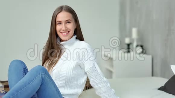 中长镜头迷人的年轻女子坐在现代卧室的床上微笑视频的预览图