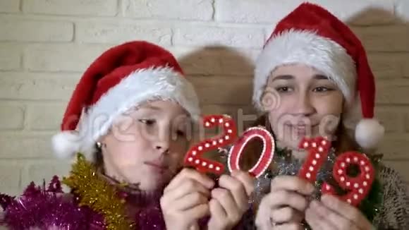 特写小朋友两个小女孩拿着2019的数字和他们一起玩他们坐在沙发上戴着红色圣诞帽视频的预览图