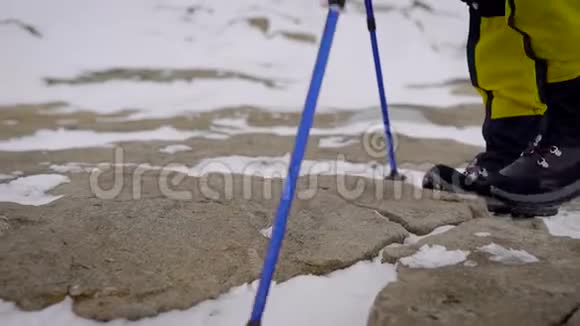 一个徒步旅行者穿着沉重的靴子腿的特写镜头和徒步旅行者在雪地和岩石上行走的徒步旅行者视频的预览图