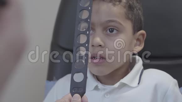 英俊的非裔美国男孩坐在医生验光师的椅子上的肖像专业眼科医生视频的预览图