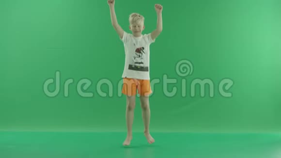 一个穿休闲服装的金发小男孩正在听音乐和跳舞他站在绿色屏幕前视频的预览图