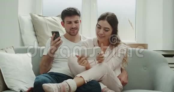 使用平板电脑夫妇从电话中订购一些东西他们穿着睡衣坐在沙发上心情愉快视频的预览图