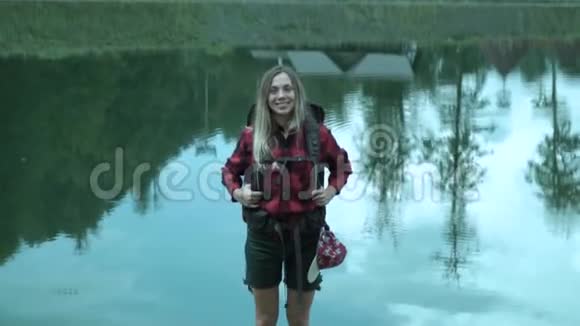 年轻可爱的少女背着背包笑着对着山湖的退出镜面视频的预览图