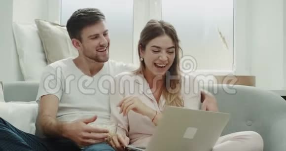 有魅力的一对夫妇周末一起吃爆米花在笔记本电脑上看一些东西视频的预览图