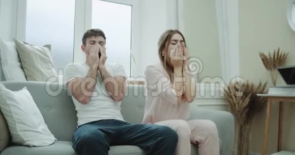 在沙发上一对年轻漂亮的夫妇穿着睡衣用纸巾流鼻涕感觉不好视频的预览图