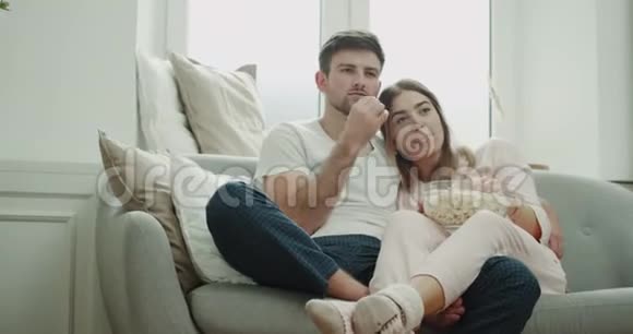 早上一起为一对夫妇谁看电视和吃爆米花睡衣坐在舒适的沙发风格视频的预览图