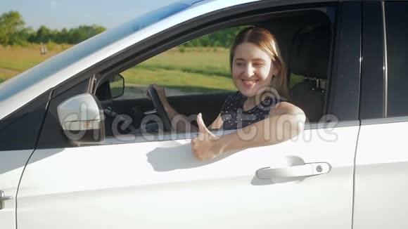 慢镜头视频美丽的微笑年轻女子驾驶汽车在乡村道路和显示拇指视频的预览图