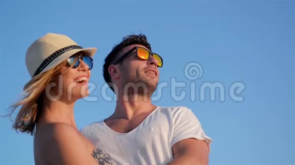 在阳光明媚的风中蓝天背景下戴着时尚太阳镜微笑快乐情侣的特写户外肖像视频的预览图