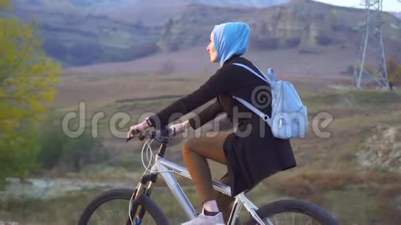 穆斯林妇女戴着头巾背着背包骑着自行车走在风景如画的路上慢悠悠视频的预览图