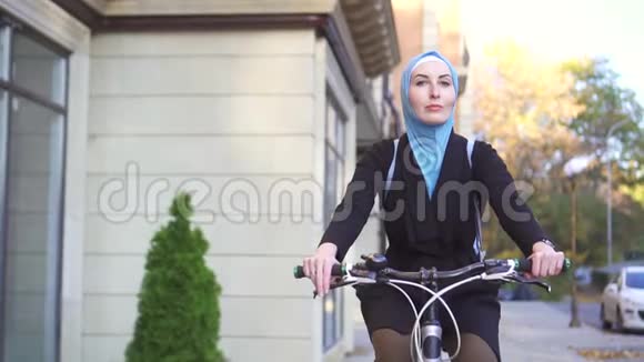 慢莫城市里骑着自行车戴着头巾的年轻穆斯林妇女画像视频的预览图