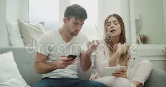流感时间一对年轻夫妇穿着睡衣坐在沙发上咳嗽感觉不舒服用平板电脑和视频的预览图