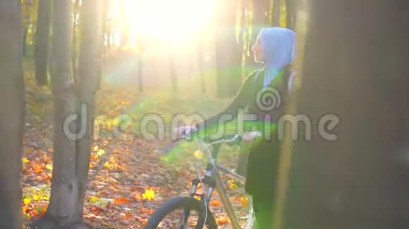 戴着头巾背着自行车背包的穆斯林妇女穿过阳光明媚的秋天公园阳光灿烂慢悠悠视频的预览图