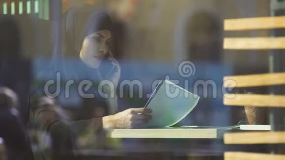 年轻迷人的穆斯林学生在咖啡馆准备考试打电话给朋友视频的预览图
