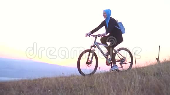 背着背包戴着头巾的穆斯林妇女在夕阳下从山上骑自行车慢吞吞的视频的预览图