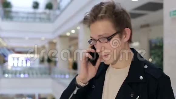 带着手机在购物中心戴眼镜的时髦年轻人的画像视频的预览图