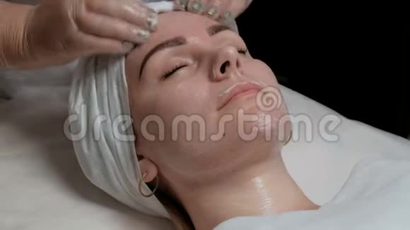 戴透明手套的美容师将面霜分布在客户的额头脸颊和下巴一个美丽的世界视频的预览图