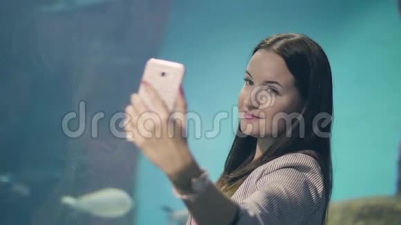 在海洋馆背景下年轻女子在手机上摆出自拍照片的姿势视频的预览图