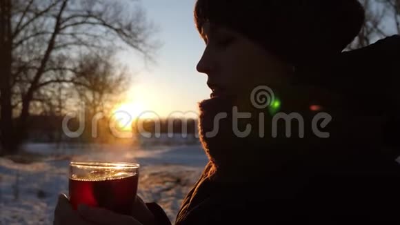 在冬天的公园里美丽的女孩在日落时手里拿着一杯热茶在寒冷的空气中蒸汽从视频的预览图