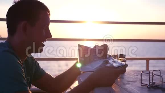 一个心情很好的年轻人坐在海滩上的咖啡馆里带着夕阳滚动着菜单想做出选择视频的预览图