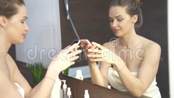 微笑的女人在浴室镜子手机上拍照视频的预览图
