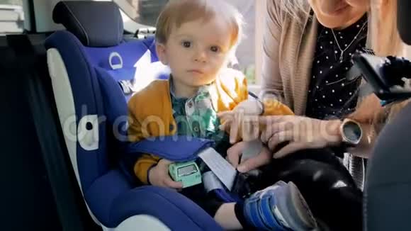 4K镜头女人把她的孩子放在孩子的汽车安全座椅运输中的安全和保护视频的预览图