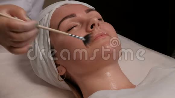女性美容师在美容中心客户脸上涂抹化妆品在那个漂亮的女孩视频的预览图