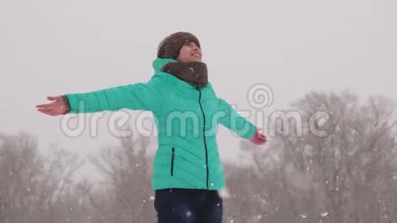 快乐的女孩在冬天的公园里捕捉雪花下雪时女孩在树林里散步慢动作视频的预览图