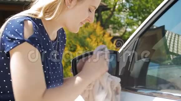 年轻女司机用超细纤维布清洁汽车上的镜子和窗户的4K镜头视频的预览图