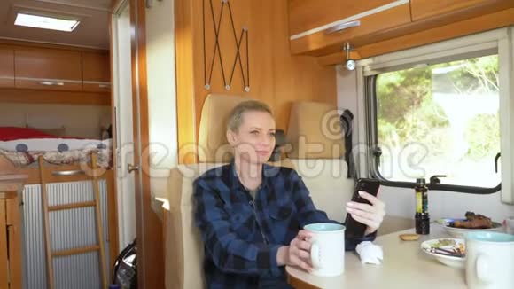 一个女人坐在汽车屋的桌子旁用手机视频的预览图
