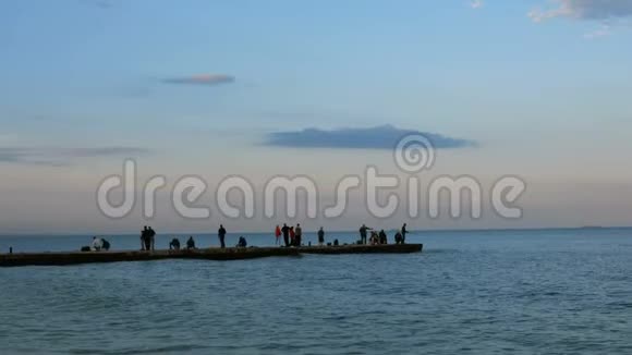 晚上在黑海人们在温暖平静的夏季傍晚沿着防波堤散步欣赏日落视频的预览图